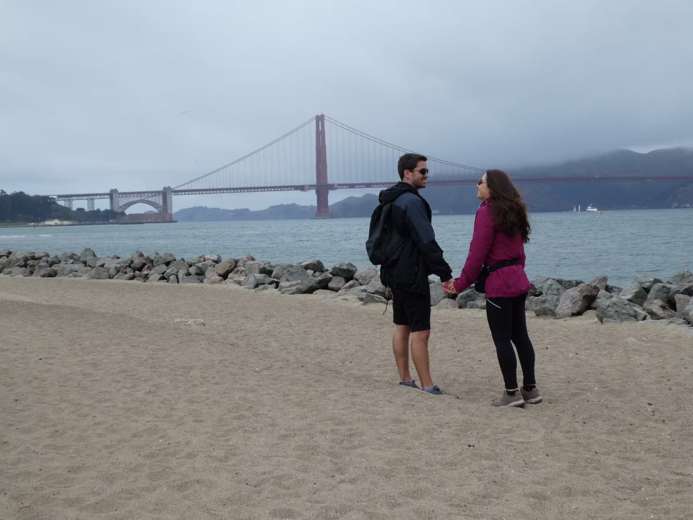 Ryne and Denise holding hands at Crissy Field in San Francisco with the Golden Gate Bridge in the background