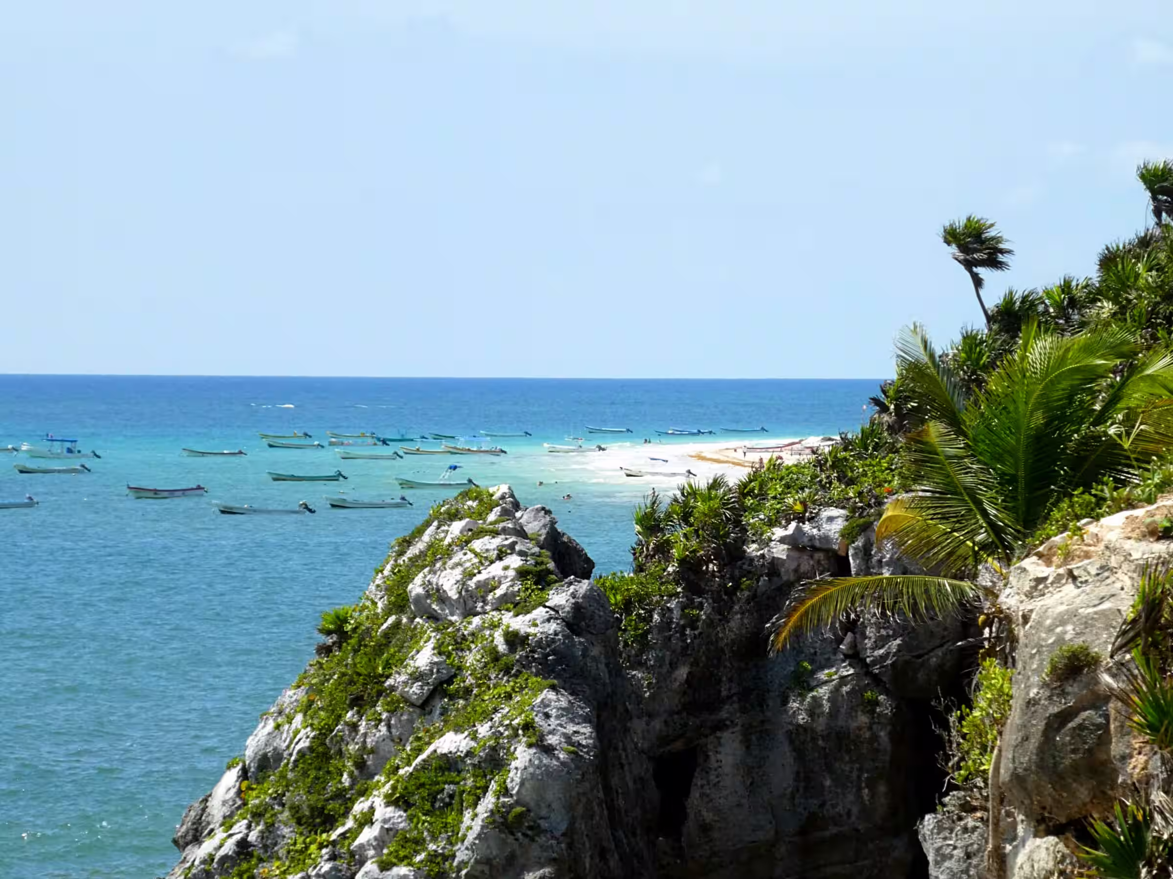 Beach ocean and boats near cliffs in Tulum