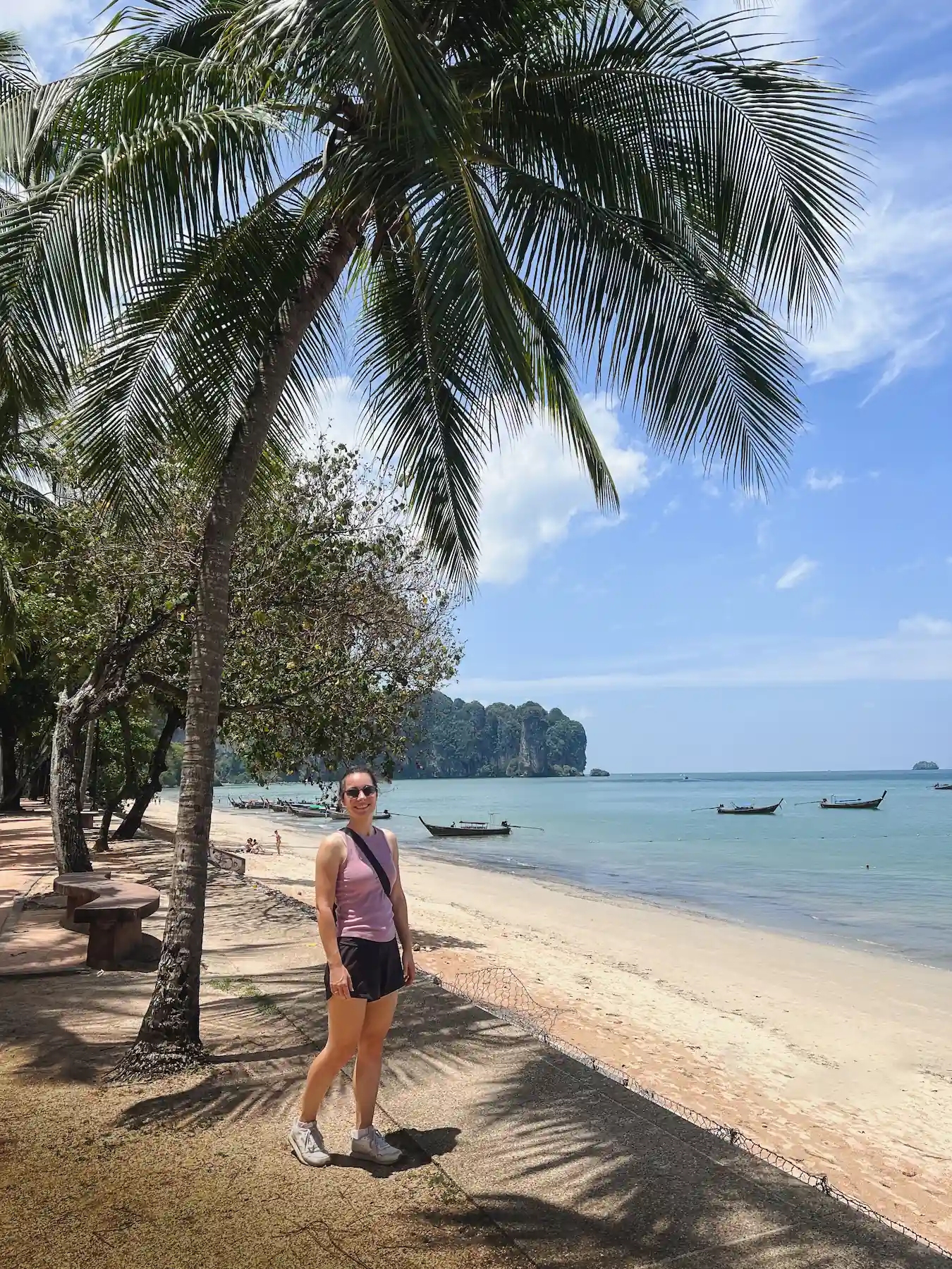 Woman smiling at Krabi beach with boats, palm trees and distant cliffs