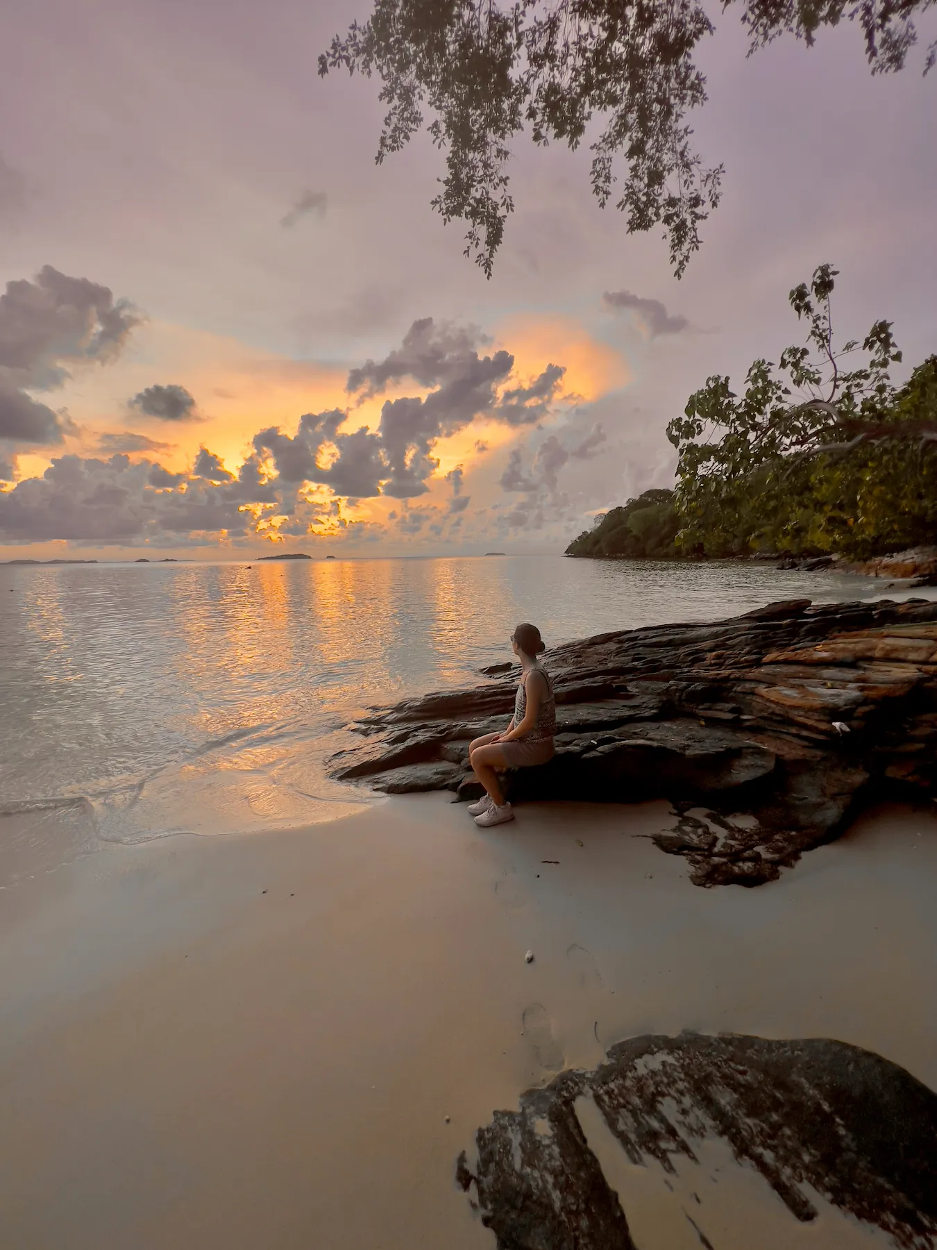 Woman sitting on rock looking at sunset