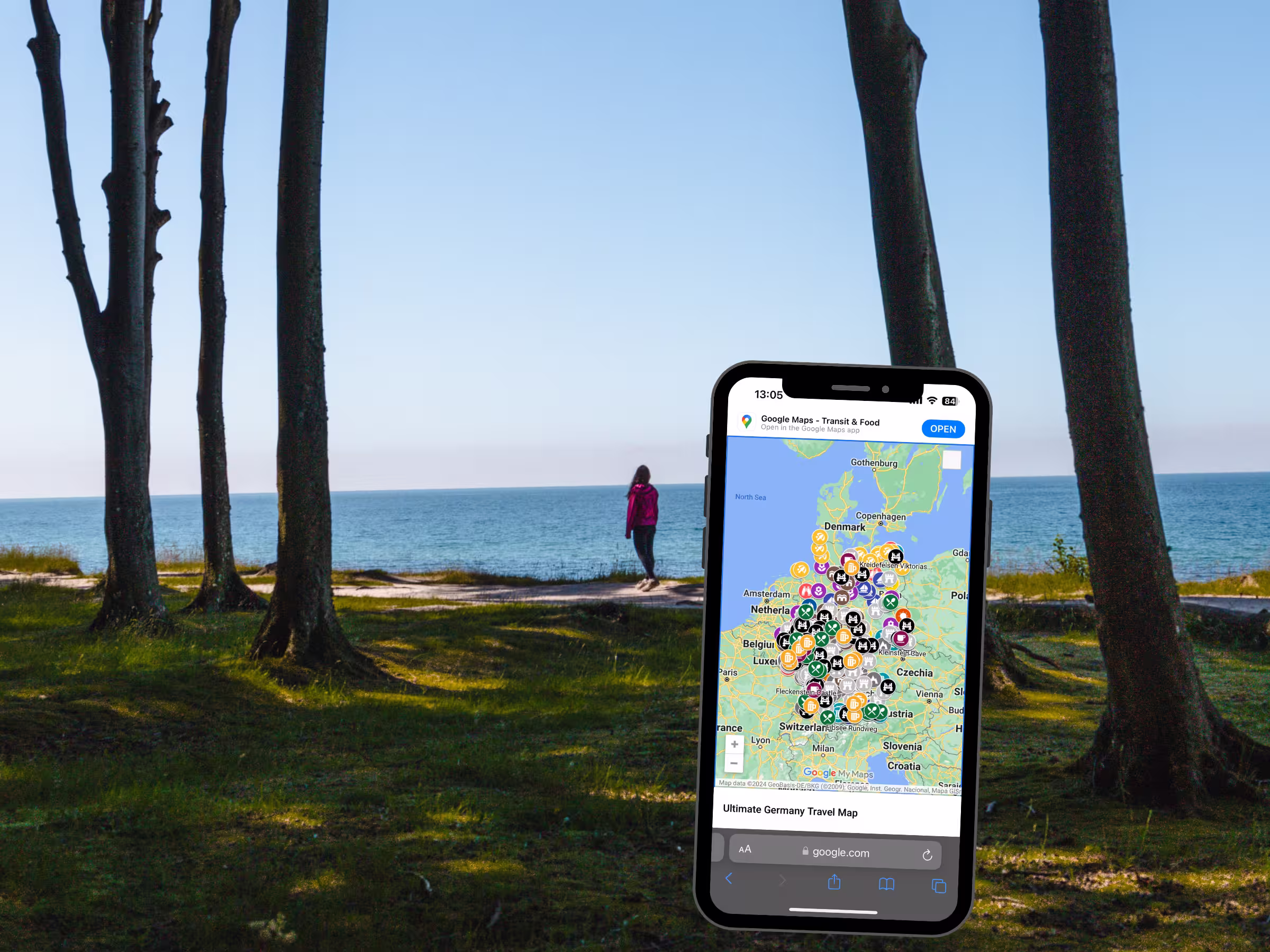 Woman in distance standing on forested cliff overlooking ocean. Phone with custom map open in foreground.