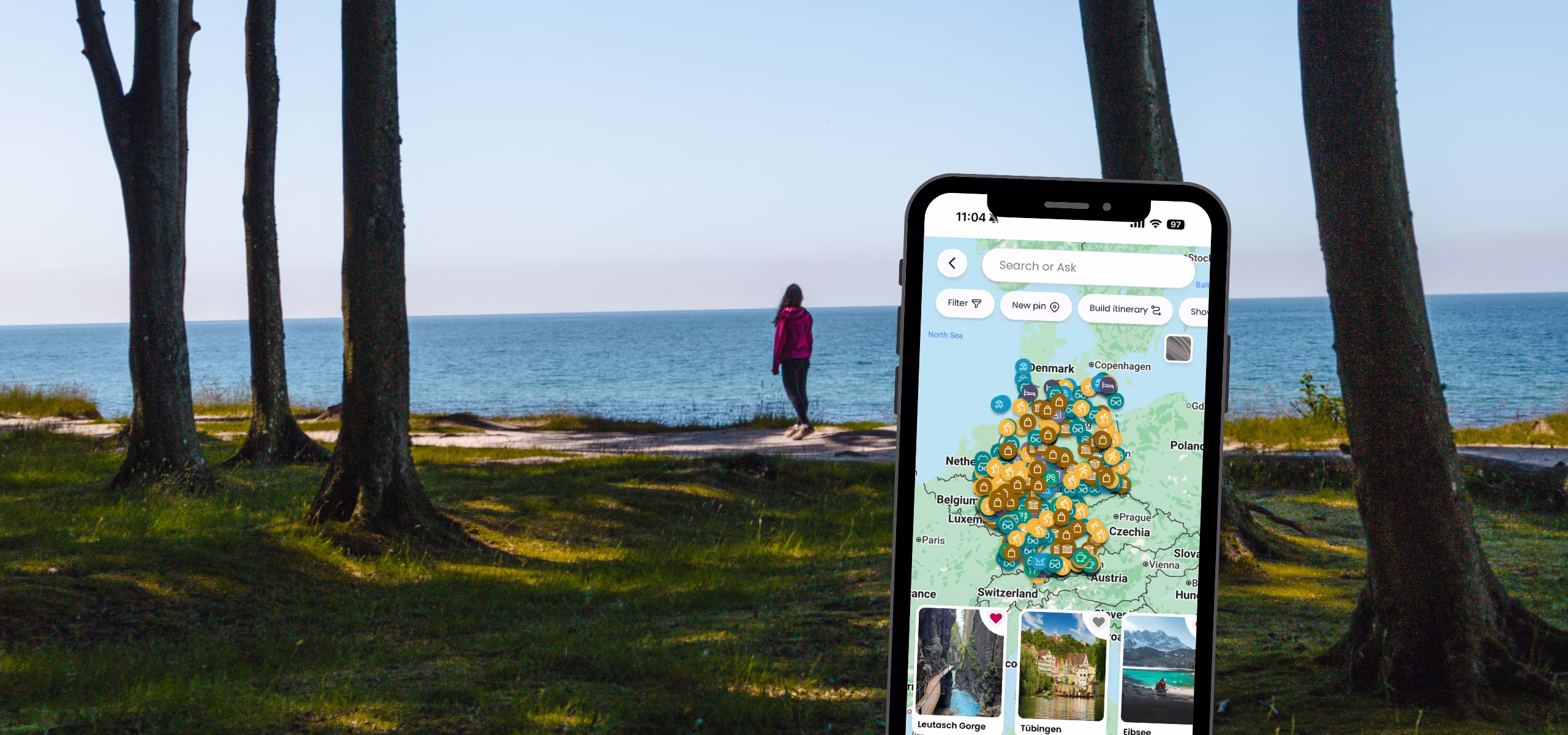 Denise in distance standing on forested cliff overlooking ocean. Phone with custom map open in foreground.